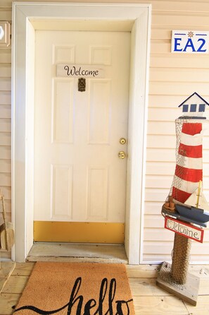 Une porte blanche avec une pancarte « Bienvenue », une boîte aux lettres avec un drapeau rayé et un paillasson sur lequel est écrit « Bonjour ».