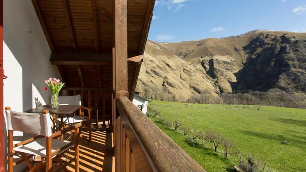 Ein Holzbalkon mit Tisch und Stühlen, der auf ein grünes Feld und Berge blickt.