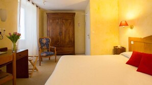 Ein Hotelzimmer mit einem Bett, einem Schreibtisch mit Stuhl, einem Kleiderschrank und einem Nachttisch mit Lampe.