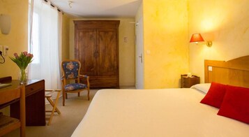 Una habitación de hotel con cama, escritorio y silla, armario y mesita de noche con lámpara.