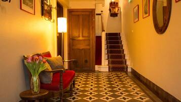 A hallway with a wooden door, a staircase with patterned steps, and a chair with a red cushion.