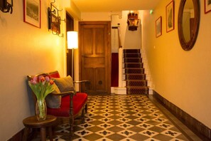 A hallway with a wooden door, a staircase with patterned steps, and a chair with a red cushion. - Logis Hôtel Etchemaïté (Doué-en-Anjou)