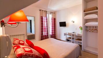 A bedroom with a bed, a bedside lamp, a TV, a desk with a chair, and a wardrobe.