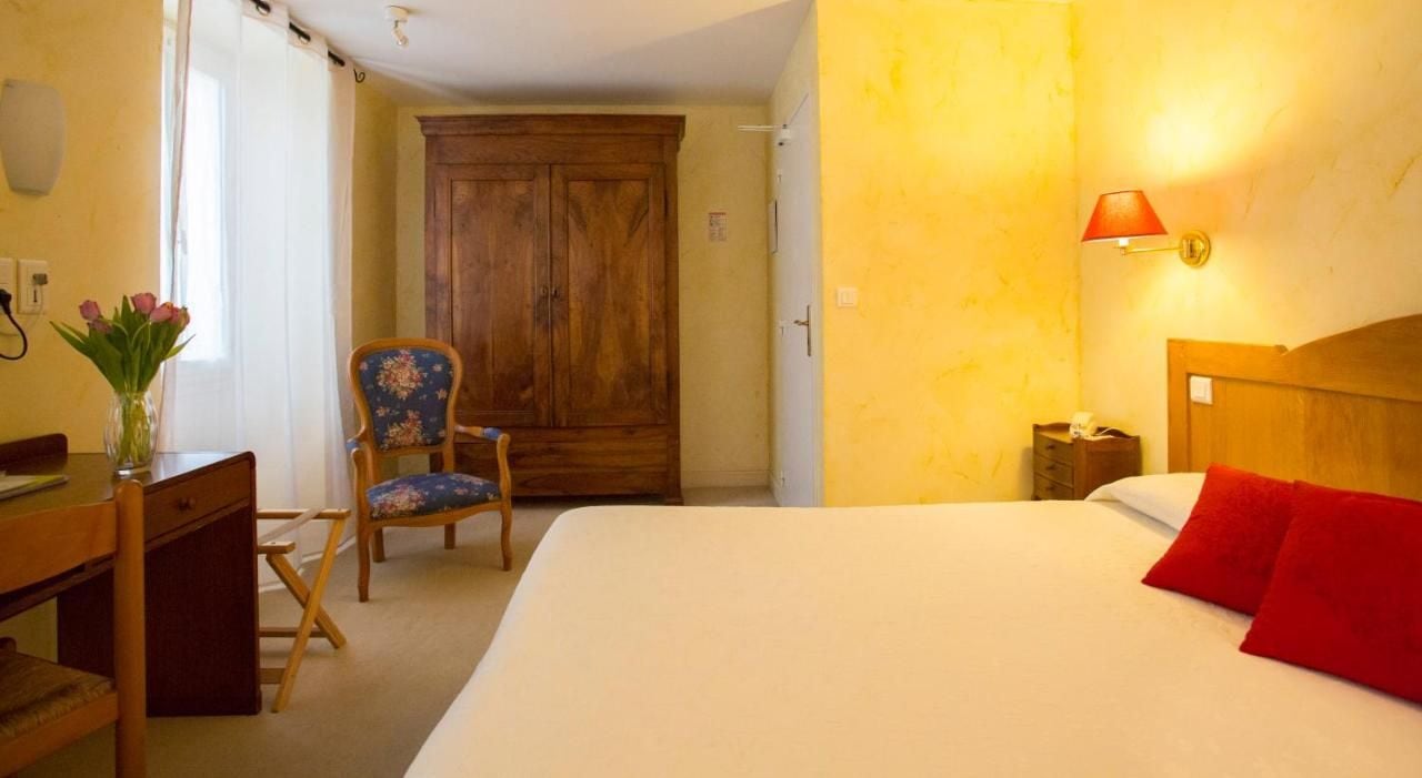 A hotel room with a bed, a desk, a chair, a wardrobe, and a lamp.