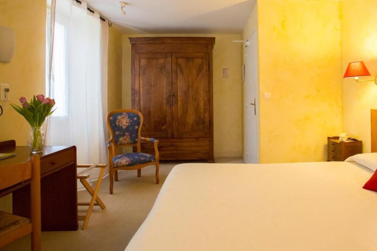 A hotel room with a bed, a desk, a chair, a wardrobe, and a lamp.