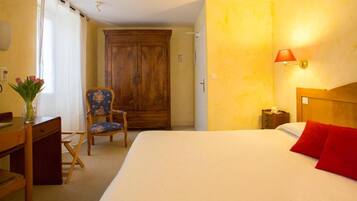 A hotel room with a bed, a desk, a chair, a wardrobe, and a lamp.