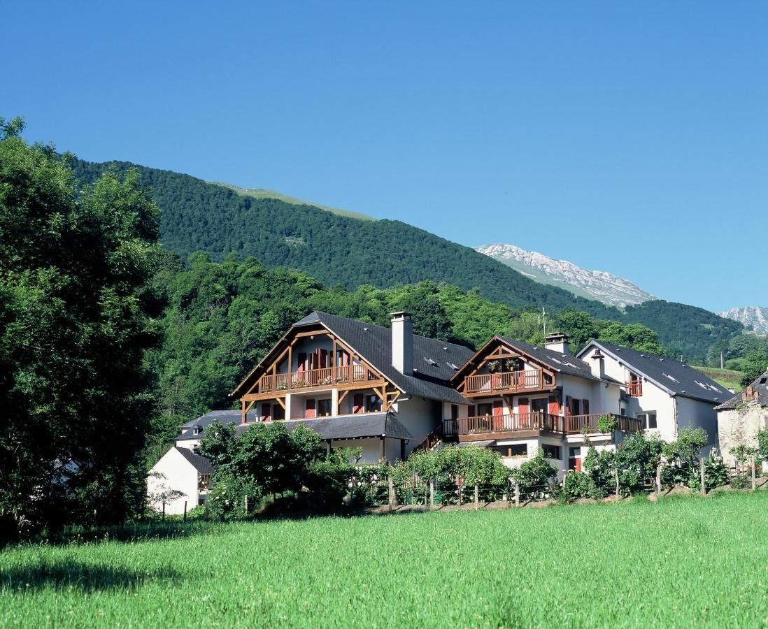 Een berghut in chaletstijl met een balkon, omgeven door weelderige begroeiing en bergen op de achtergrond.