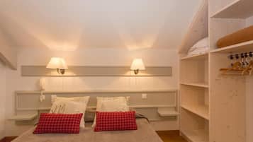 A hotel room with a bed, bedside lamps, a wardrobe, and a shelf with folded towels.