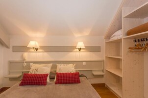 Un dormitorio con cama, dos lámparas de noche, un armario y una estantería con ropa doblada.