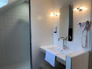 A modern bathroom with a glass shower enclosure, a white sink with a towel, a mirror with lights, and a hairdryer mounted on the wall. - Logis Hôtel Etchemaïté (Doué-en-Anjou)