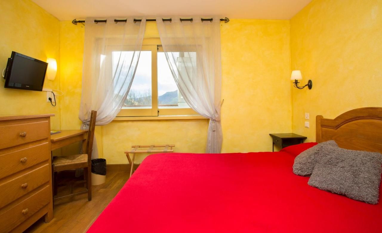 Una camera da letto con un letto, una scrivania, una sedia, una televisione e una finestra con tende.