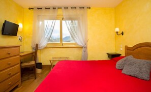 Un dormitorio con cama, escritorio, silla, televisor y ventana con cortinas.