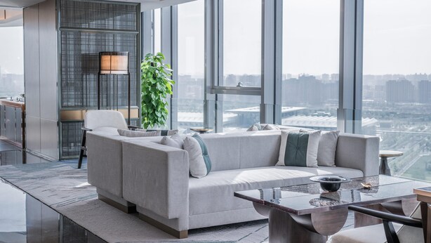 A modern living room with a sofa, a coffee table, and a large window offering a city view.