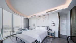 A modern hotel room with a large bed, a bench, a desk, and a view of the city.
