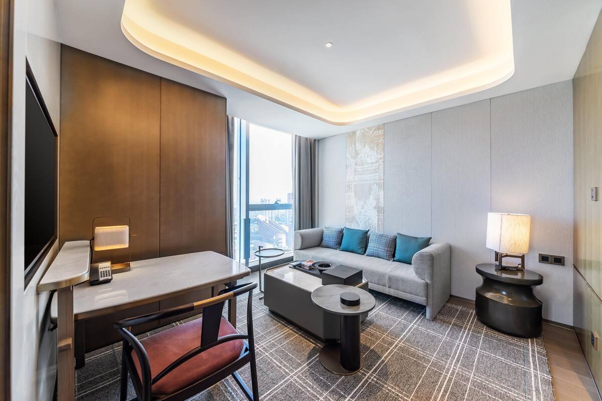 A modern hotel room with a desk, sofa, and a view of the city.