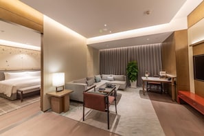 Habitació d'hotel moderna amb llit, sofà, zona de menjador i televisió.