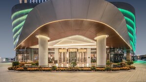A modern hotel with a curved facade, large columns, and a well-lit entrance.