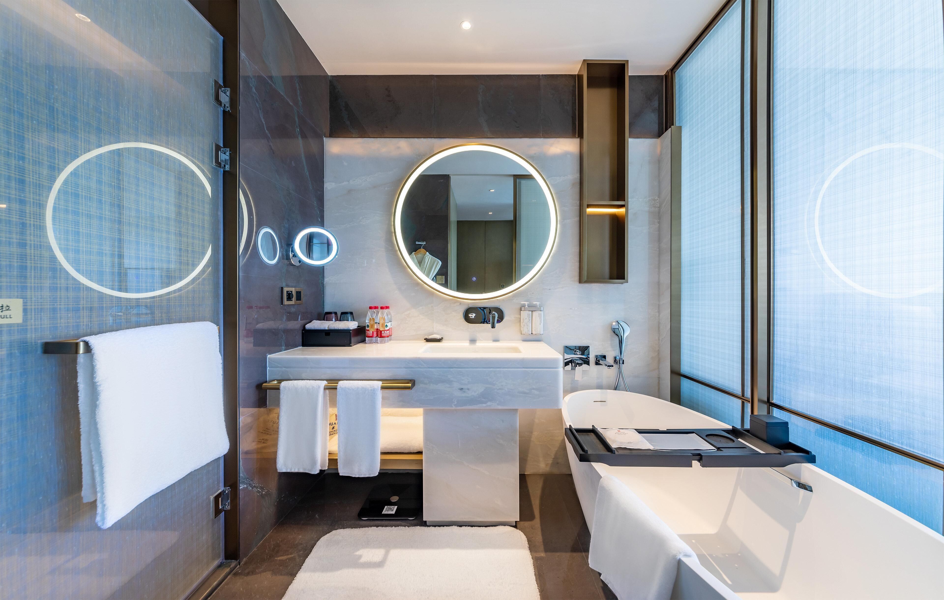 A modern bathroom with a large mirror, a bathtub, a sink, and a towel rack.