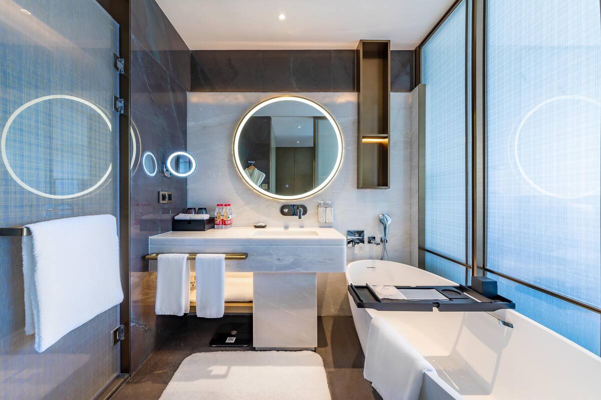 A modern bathroom with a large mirror, a bathtub, a sink, and a towel rack.