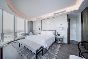 Una habitació d'hotel moderna amb un llit gran, una banca, un escriptori i vistes a la ciutat.