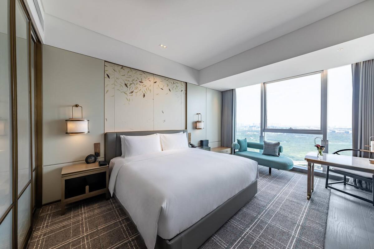 A modern hotel room with a large bed, a desk, and a view of the city.