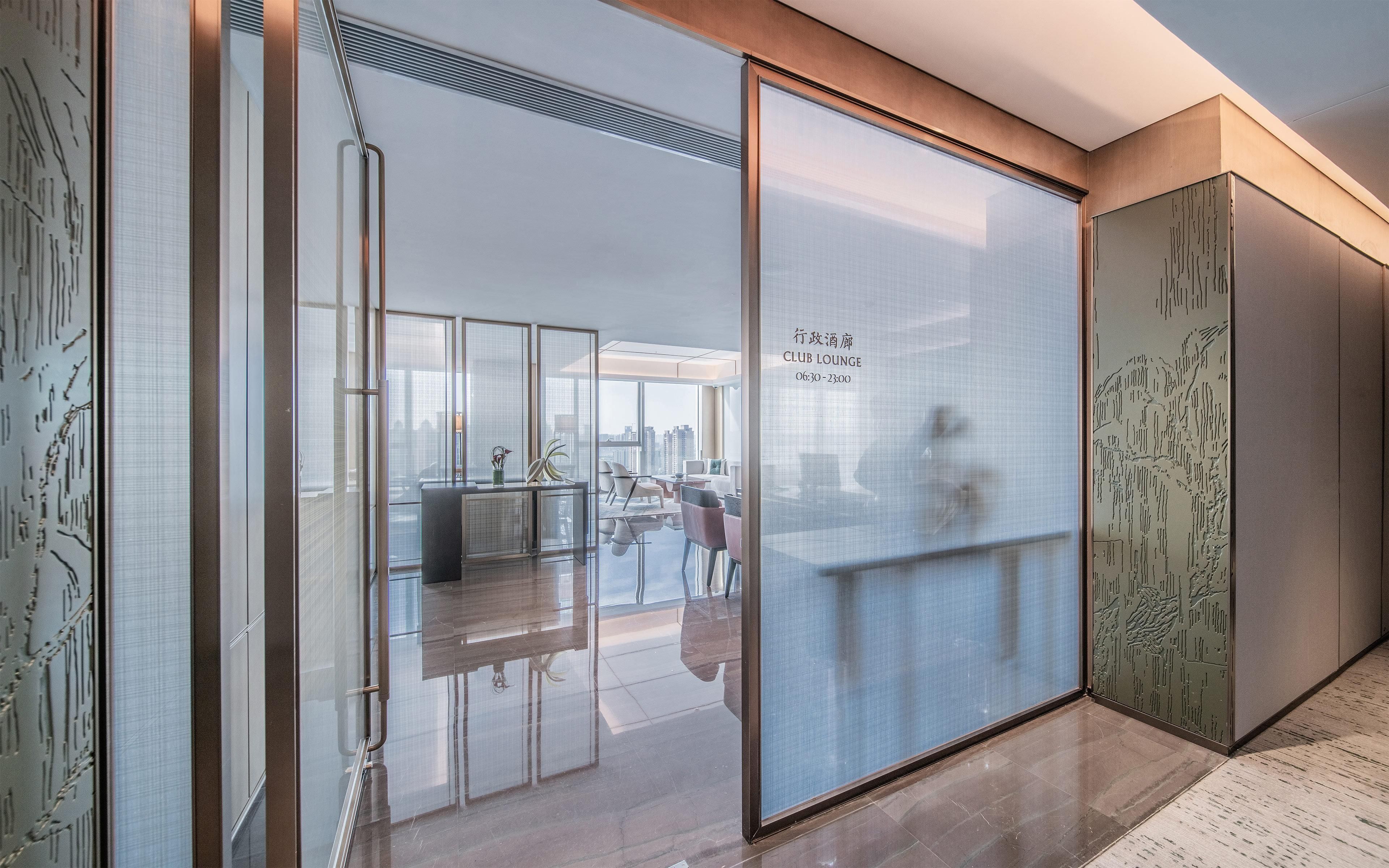 A modern lounge area with a glass partition, a seating area with chairs and tables, and a city view.