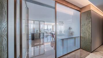 A modern lounge area with a glass partition, a seating area with chairs and tables, and a city view.
