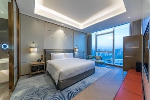 Ein modernes Hotelzimmer mit einem großen Bett, einer Sitzecke mit Blick und einer Stadtansicht durch die Fenster.