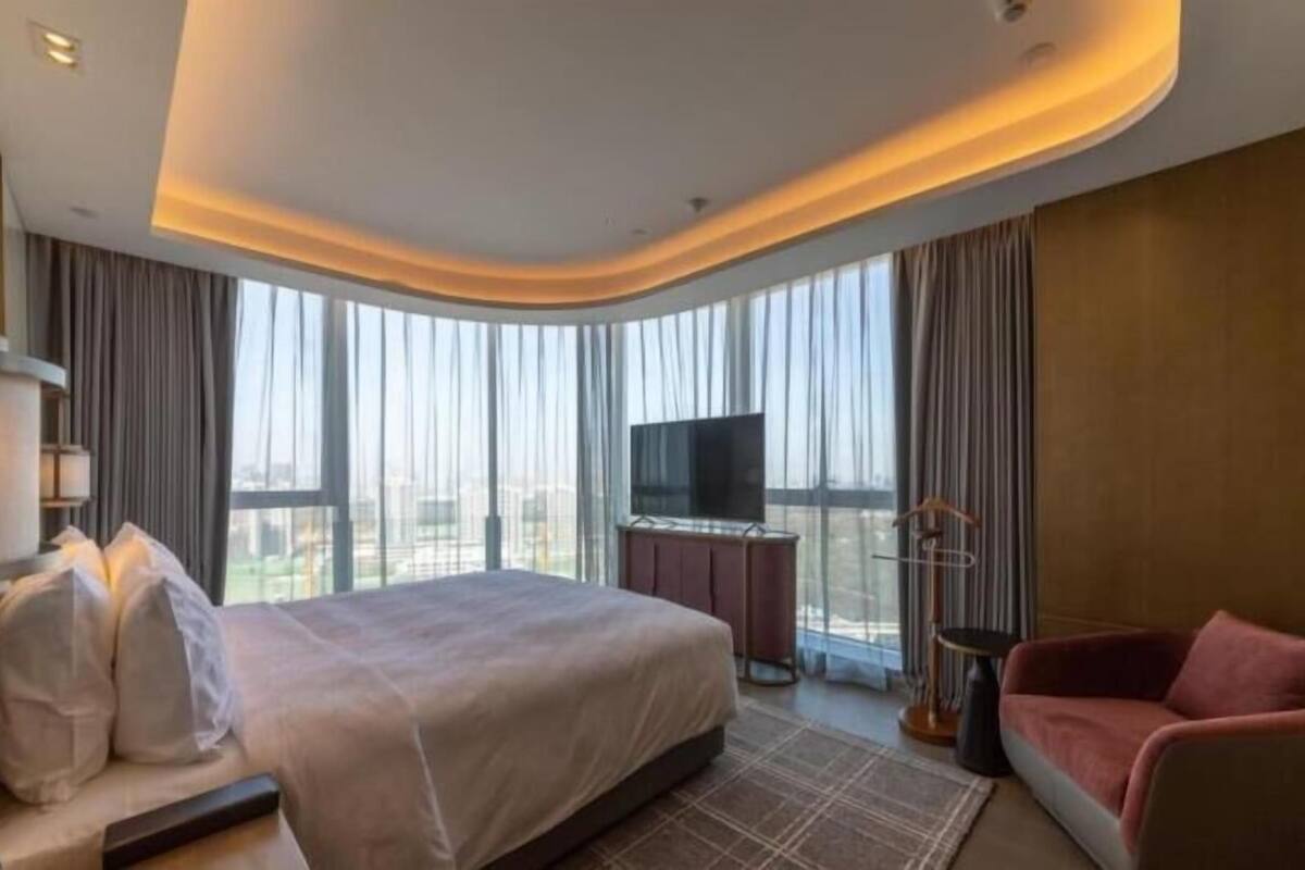 A hotel room with a bed, a TV, a chair, and a view of the city.