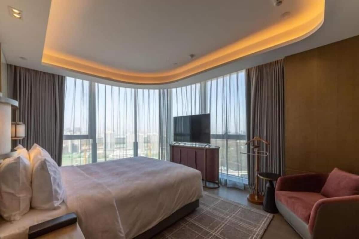 A hotel room with a bed, a TV, a chair, and a view of the city.