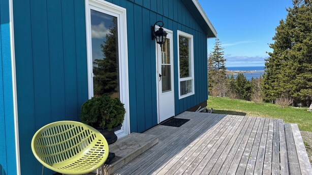 A blue house with a wooden deck, a yellow chair, and a small potted plant. - Margaree-a-ville Cottage (Margaree Harbour)