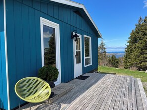 A blue house with a wooden deck, a yellow chair, and a small potted plant. - Margaree-a-ville Cottage (Margaree Harbour)