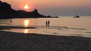 A beach at sunset with calm waters, a boat in the distance, and rocky cliffs. - Margaree-a-ville Cottage (Margaree Harbour)