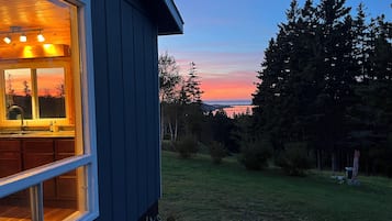 A house with a visible kitchen area, a window overlooking a grassy yard, and a view of trees and a sunset.
