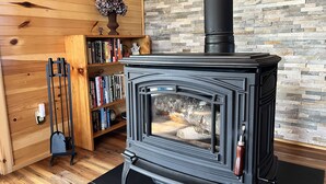 A wood-burning stove in a room with a stone wall and wooden paneling. - Margaree-a-ville Cottage (Margaree Harbour)