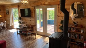 A wooden cabin interior with a fireplace, a television, a dining area, and a bookshelf. - Margaree-a-ville Cottage (Margaree Harbour)