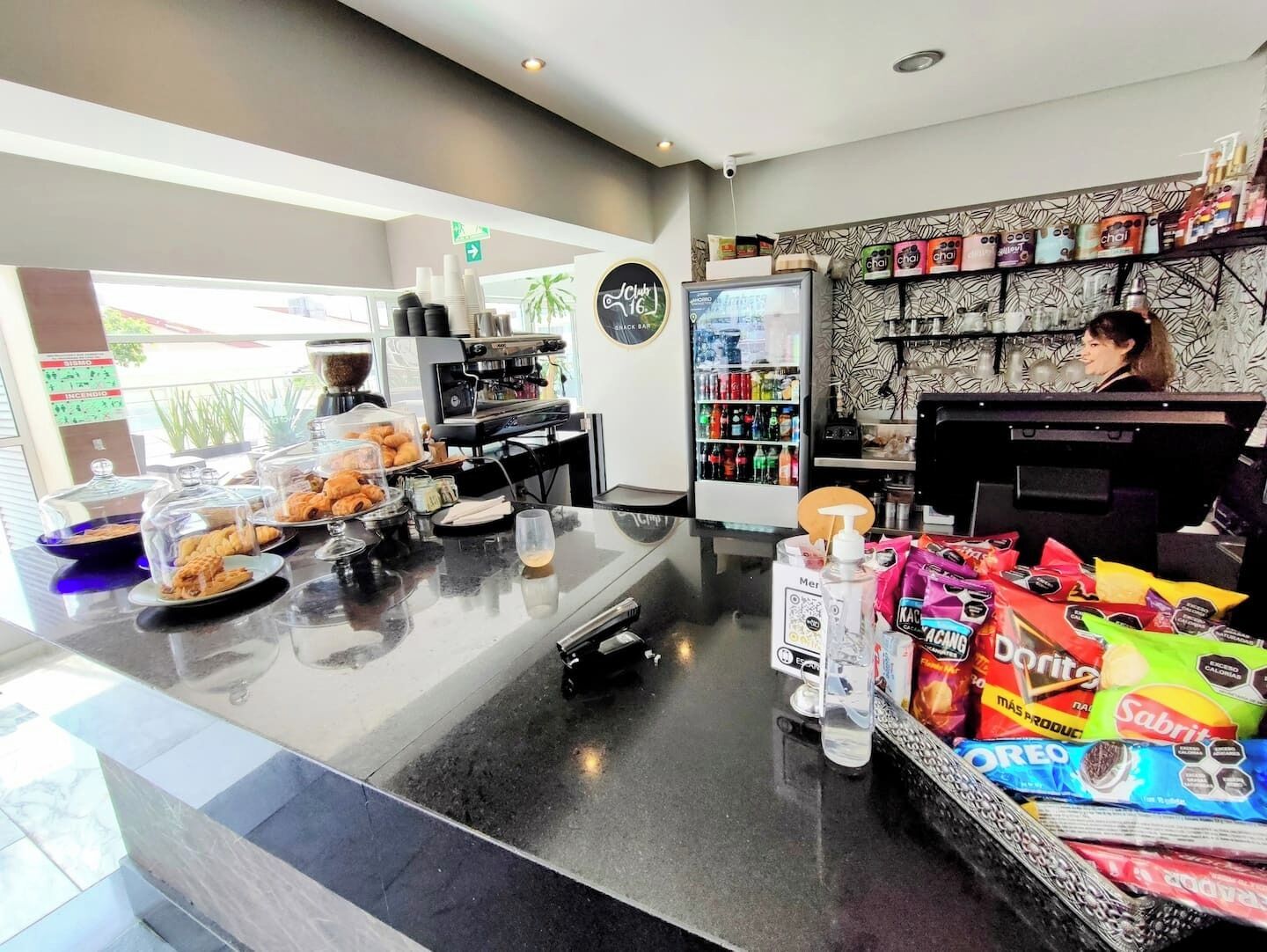 Ein Café mit einer Kaffeemaschine, einem mit Getränken gefüllten Kühlschrank und einer Auswahl an Snacks.