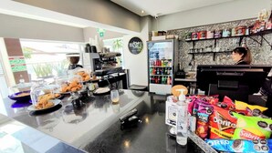 Ein Café mit einer Kaffeemaschine, einem mit Getränken gefüllten Kühlschrank und einer Auswahl an Snacks.