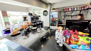 Ein Café mit einer Kaffeemaschine, einem mit Getränken gefüllten Kühlschrank und einer Auswahl an Snacks.