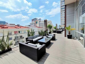 Relax on the rooftop terrace with comfortable sofas and a glass coffee table, surrounded by lush greenery and a city view.