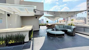 Eine Dachterrasse mit einer gebogenen Couch, einem kleinen Tisch und Kübelpflanzen.