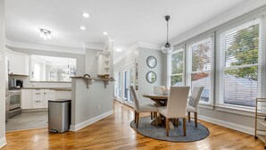 Una cocina moderna con armarios blancos, un refrigerador de acero inoxidable y una zona de comedor con una mesa redonda y sillas.