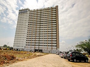 Un hotel de varios pisos con un letrero llamativo, un estacionamiento con varios coches y un camino de tierra que conduce a la entrada.