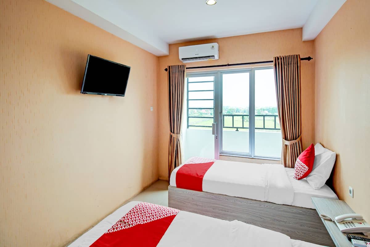 A hotel room with two beds, a television, an air conditioning unit, and a balcony with curtains.