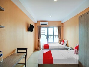 Ein Hotelzimmer mit zwei Betten, einem an der Wand befestigten Fernseher, einem Schreibtisch mit Stuhl und einem Fenster mit Vorhängen.