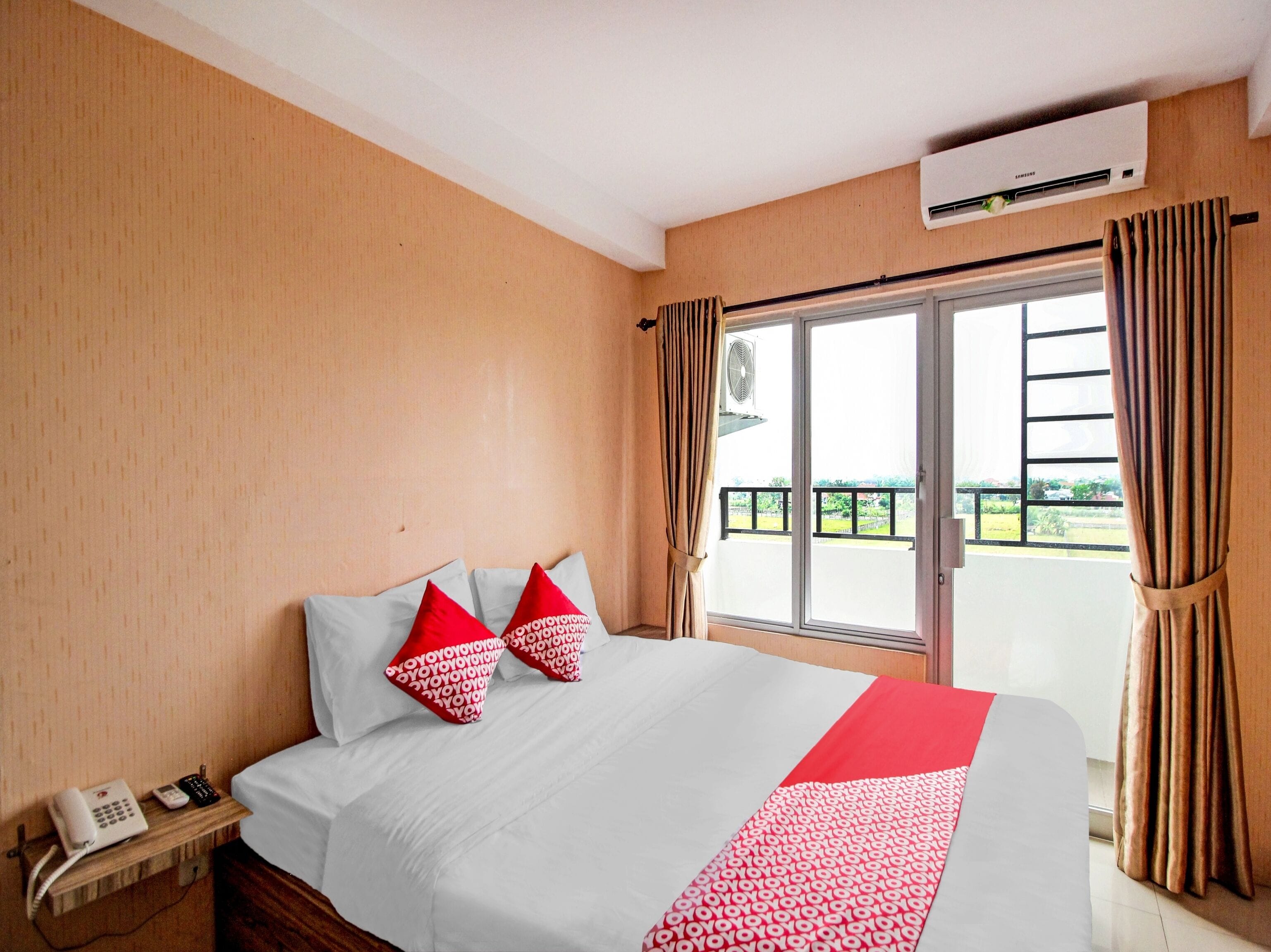 A hotel room with a bed, a telephone, an air conditioning unit, and a view of the outside.