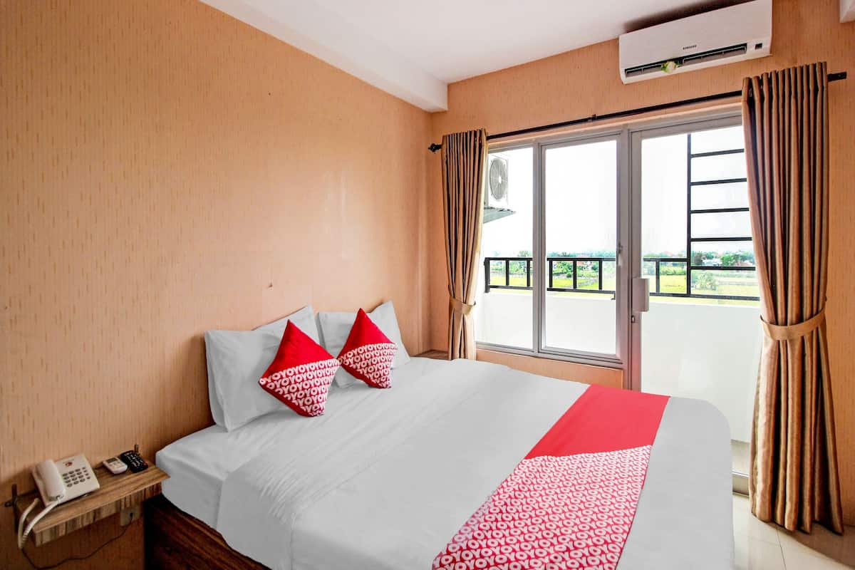 A hotel room with a bed, a telephone, an air conditioning unit, and a view of the outside.