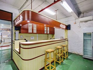 A coffee shop counter with a wooden finish, a coffee sign, and three wooden stools. - Super OYO 90245 Tridasa (Medan)