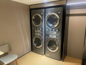 A laundry room with four stacked washing machines, a chair, and a wooden floor.