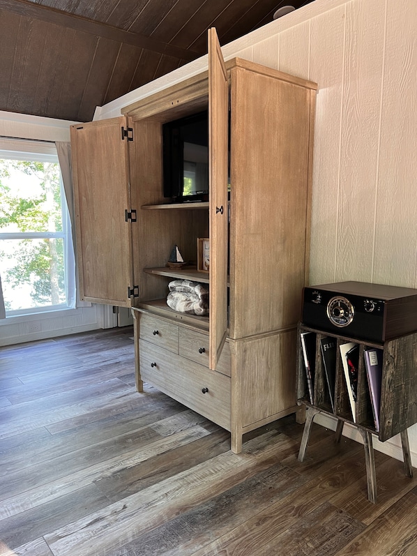 A wooden cabinet with open doors revealing a television, a framed picture, and a small shelf with a blanket.